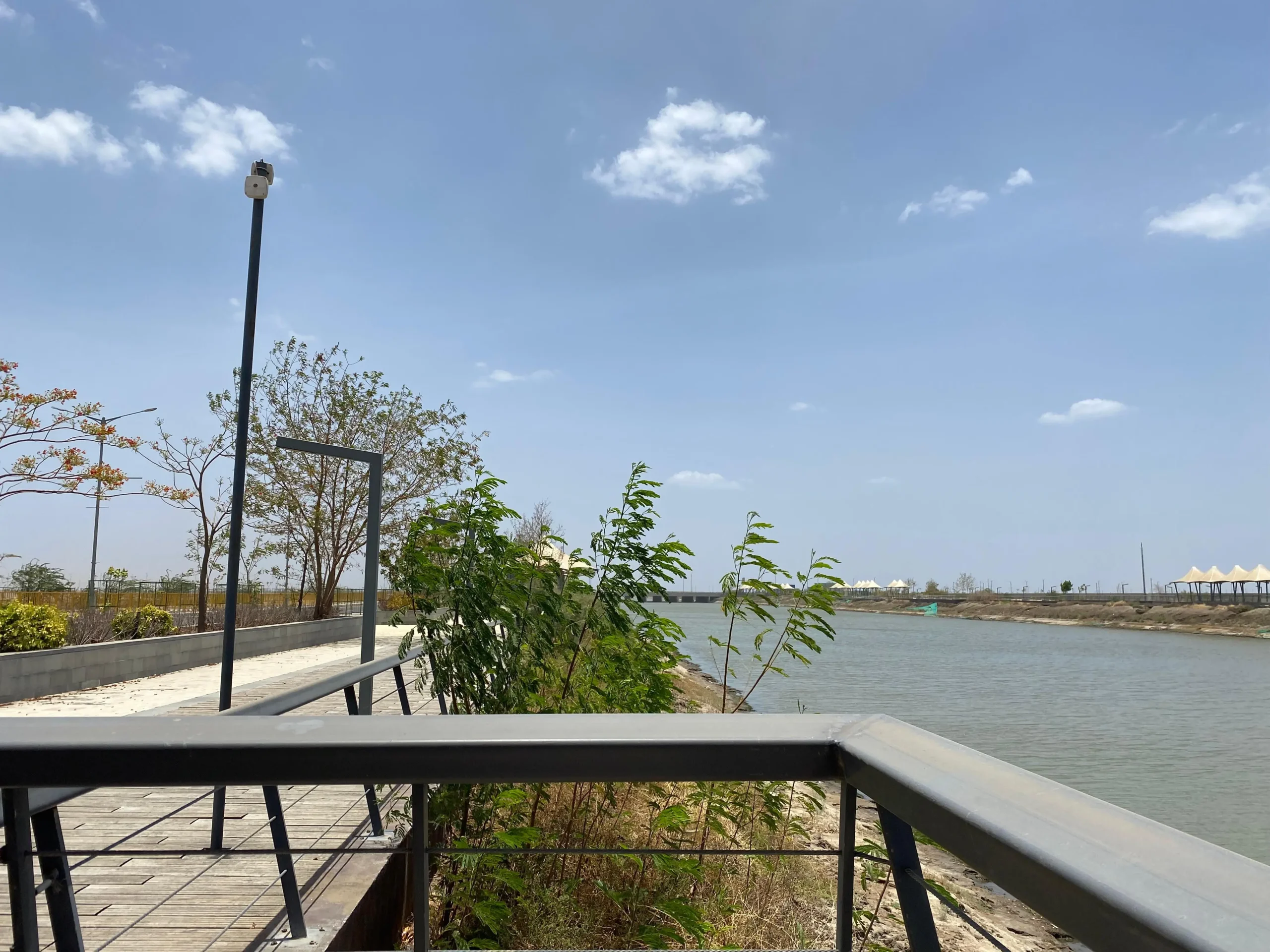 Dholera SIR smart city Riverfront a walkway with a metal railing next to a body of water , Urban NXT Developers